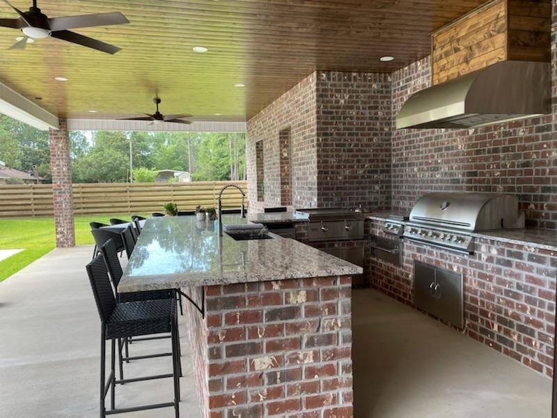 Completed outdoor kitchen with brick surround and grill under a covered patio
