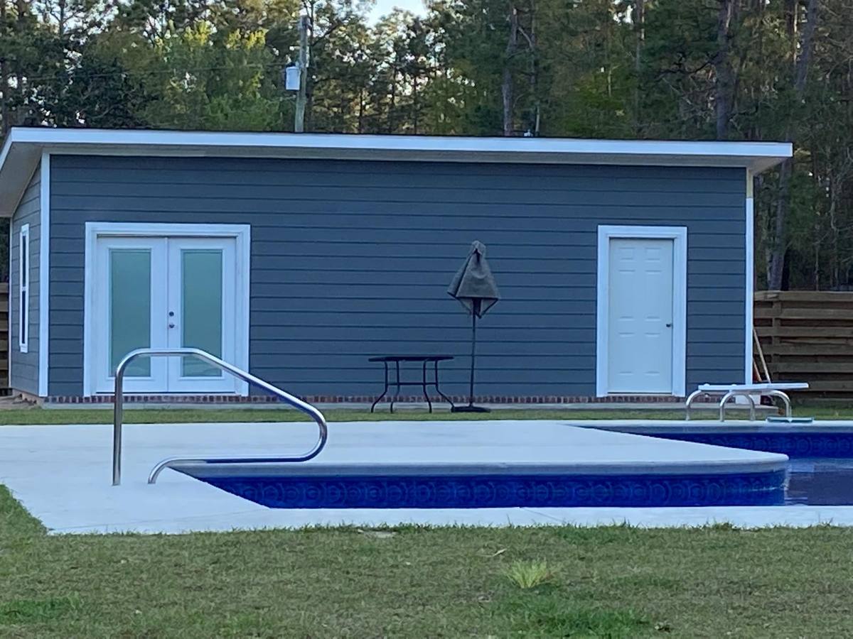 Completed pool house with dark siding next to an in-ground pool